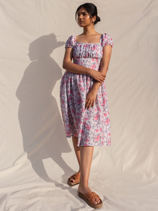 Woman wearing a floral dress standing against a plain background