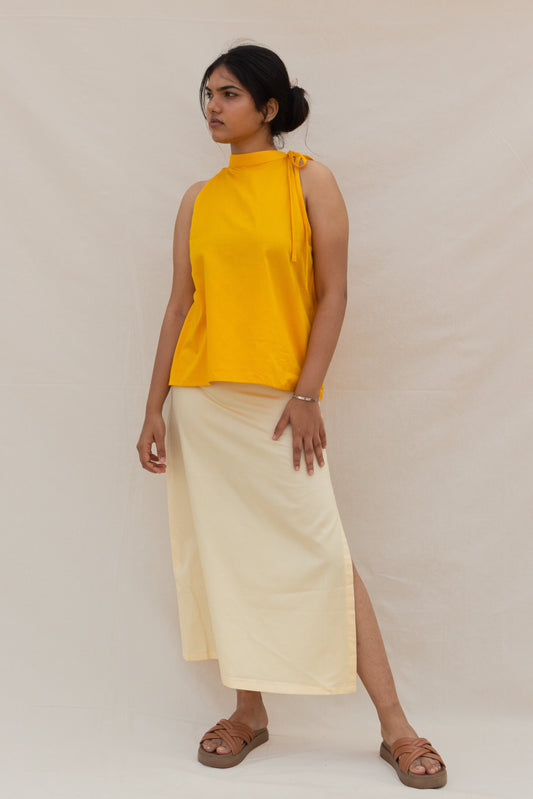 Woman wearing a yellow sleeveless top and light-colored skirt on a plain background